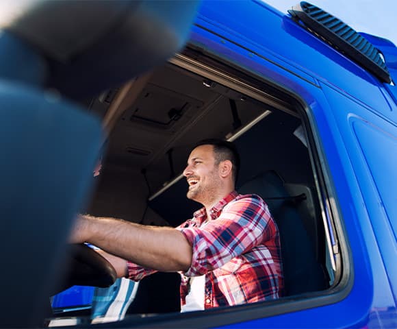 Homem sorrindo enquanto está dentro da cabine de caminhão dirigindo