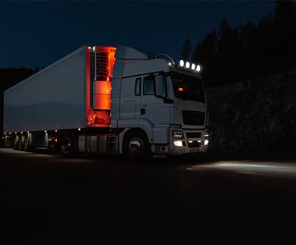 Caminhão seguindo viagem um uma estrada à noite com os faróis acesos